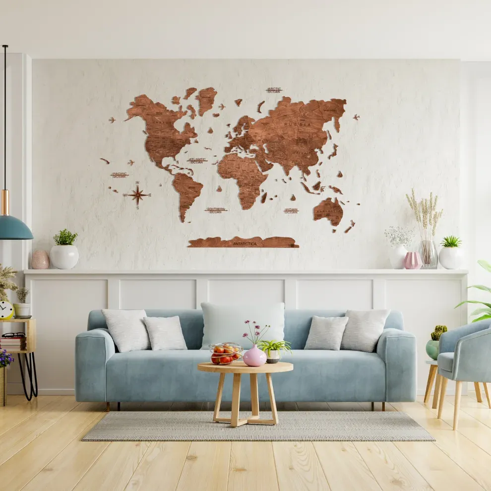 A dark-brown GeoArte wooden world map with labels, compass and Antarctica above a pale blue sofa
