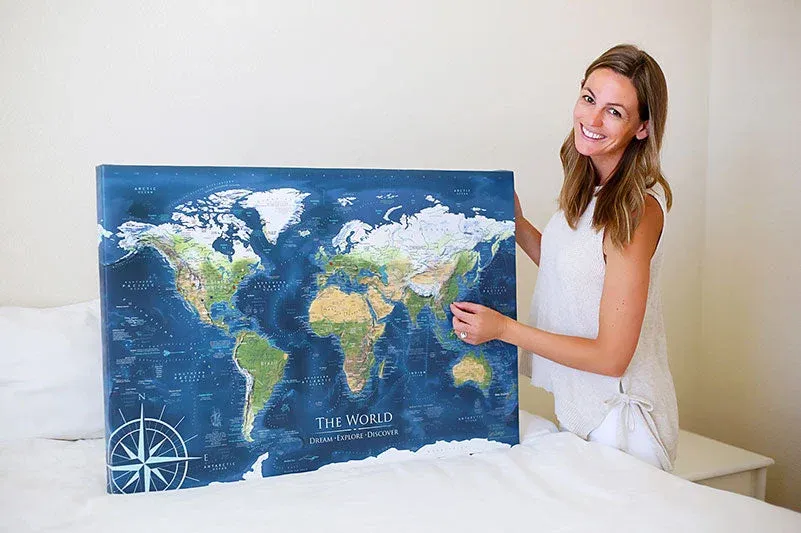 Woman holding a blue GeoJango world map on a wrapped canvas with its edge visible