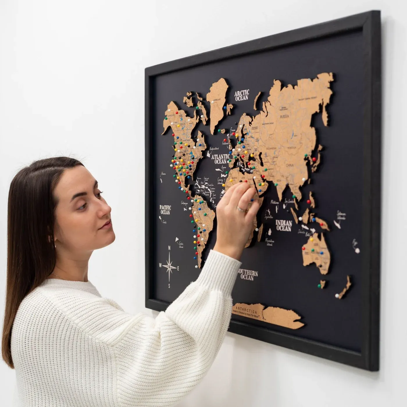Person pinning memories to a cork world map on a dark framed panel