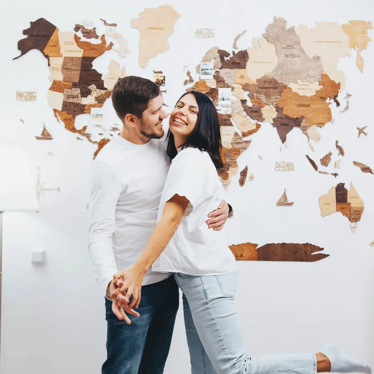 Enjoy The Wood multitone wooden world map installed on a white wall behind two people