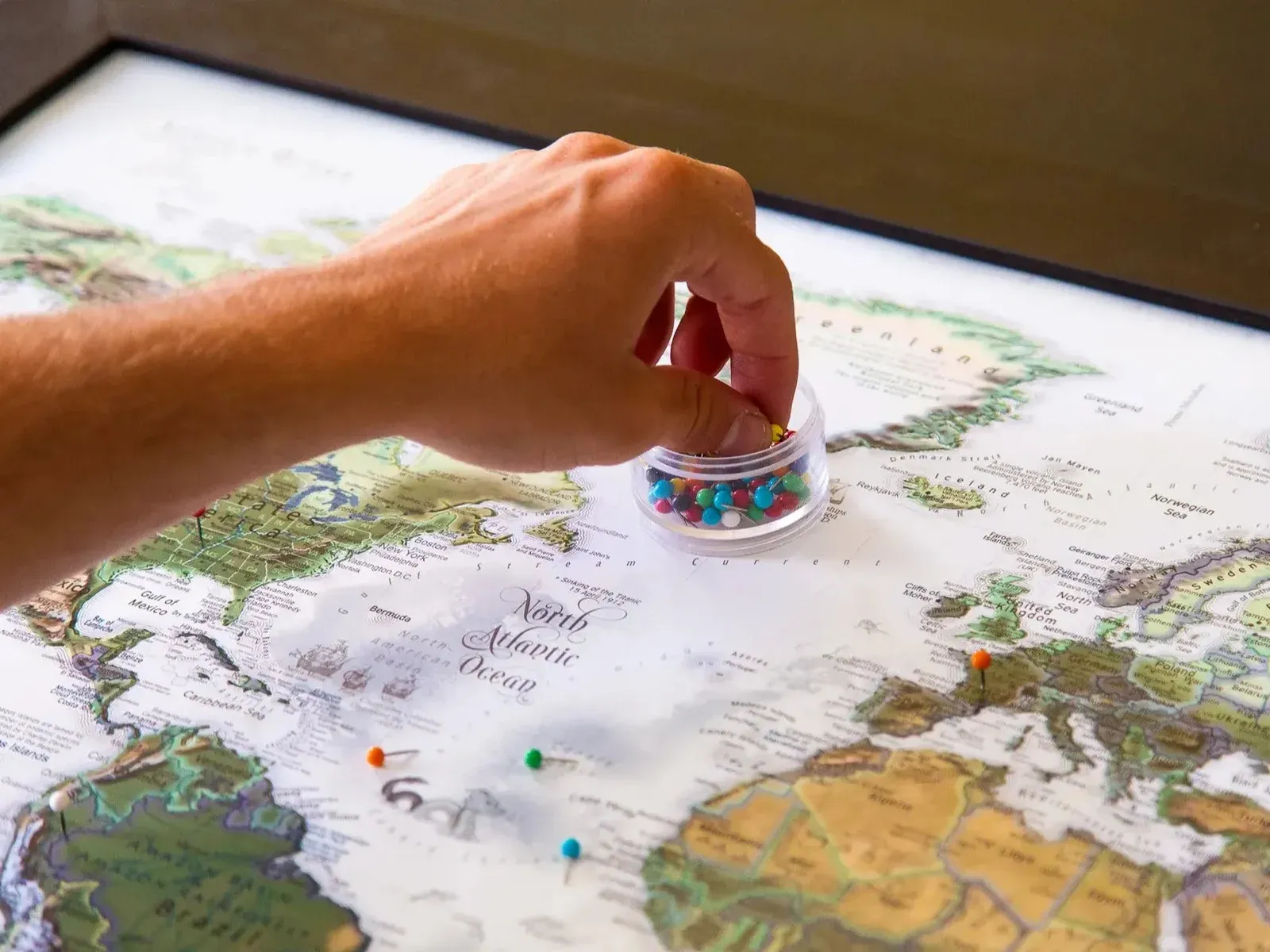 Hand choosing a marker beside pins on a detailed GeoJango printed world map